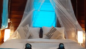 A bed with a white canopy, blue bedding, and two bedside tables with decorative items. - Baan Klong Kleng (Ranong)