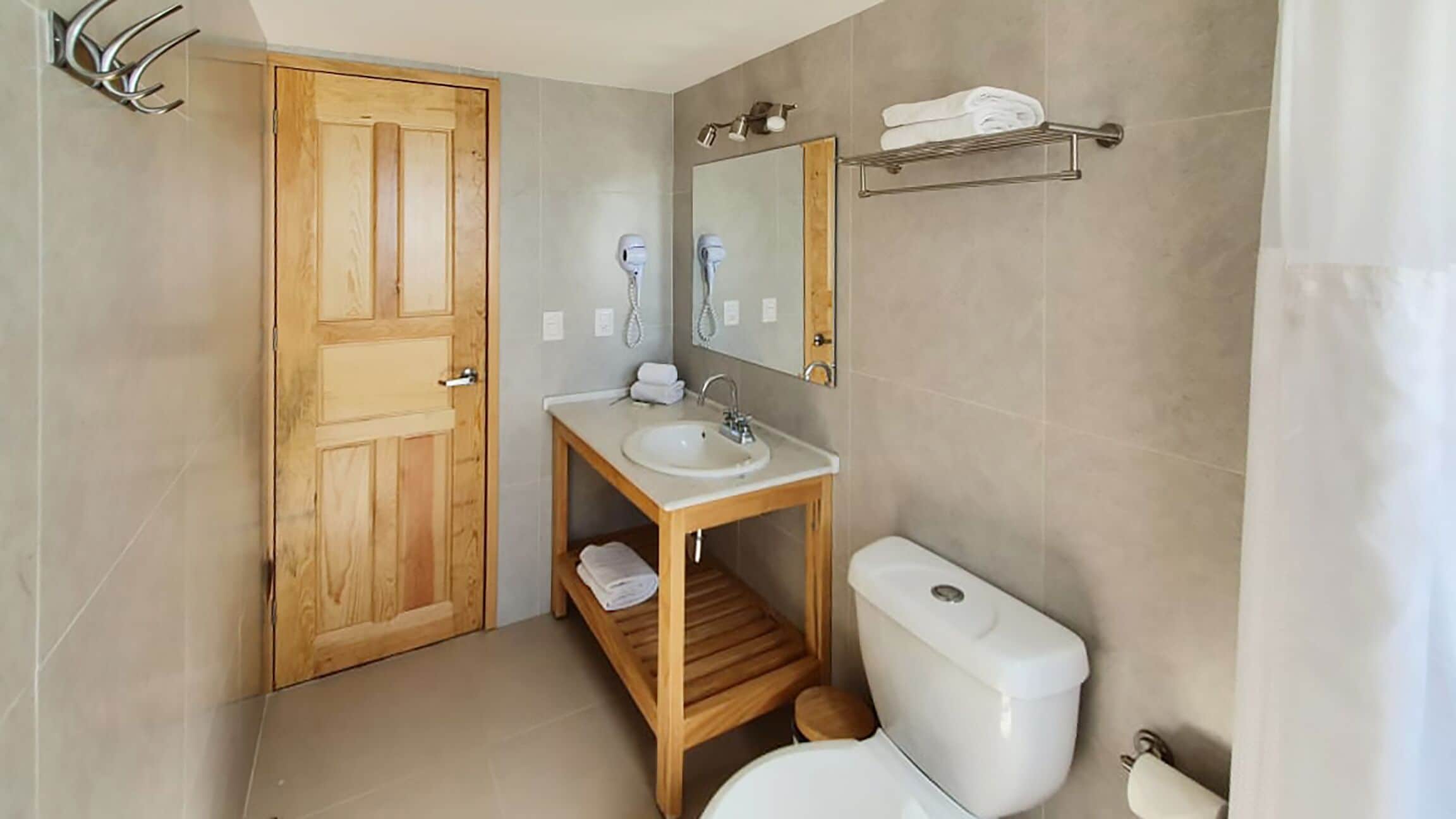 A bathroom with a wooden door, a sink with a mirror, a toilet, and a towel rack.