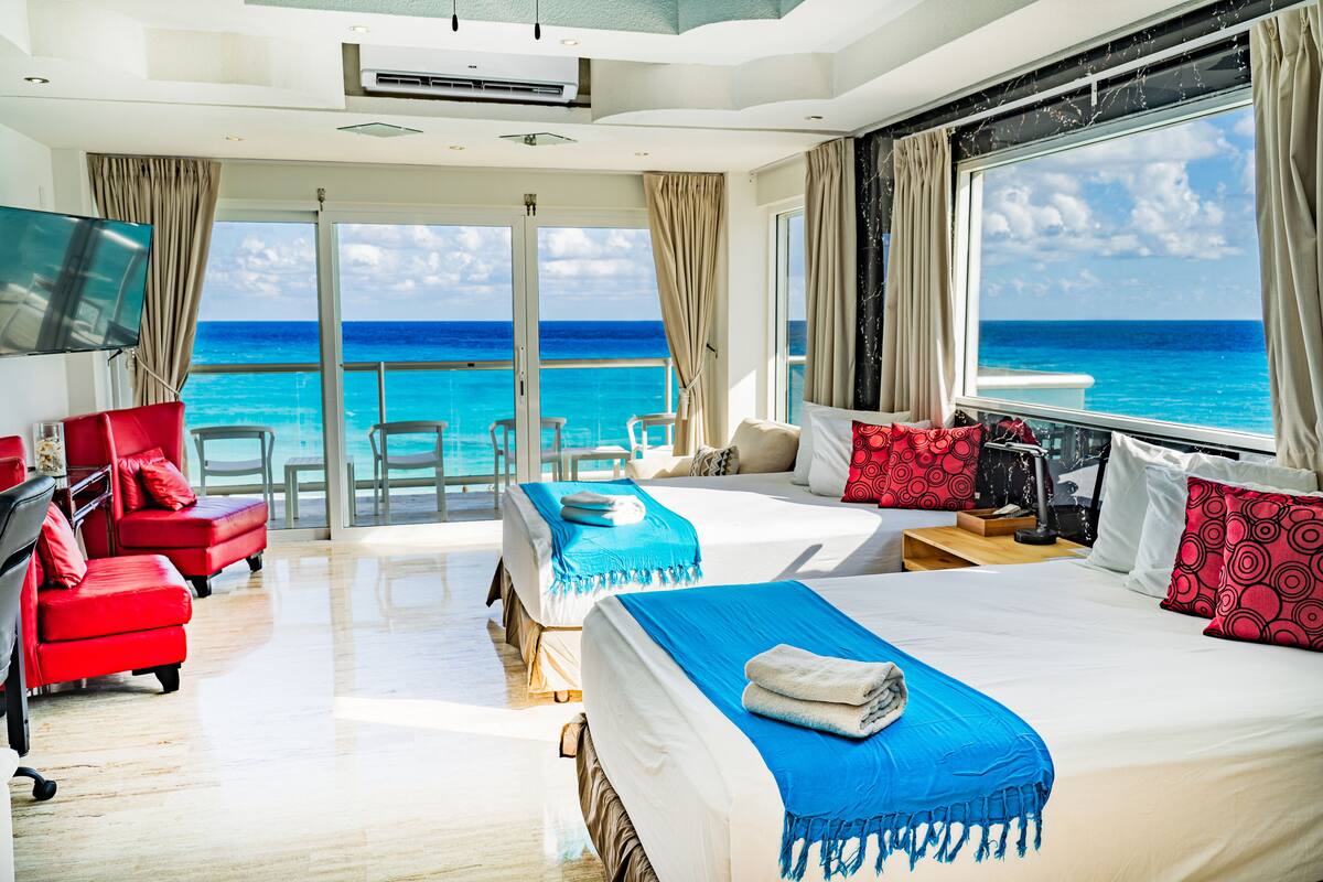 A hotel room with a balcony, a bed with blue and red bedding, a red armchair, and a TV.