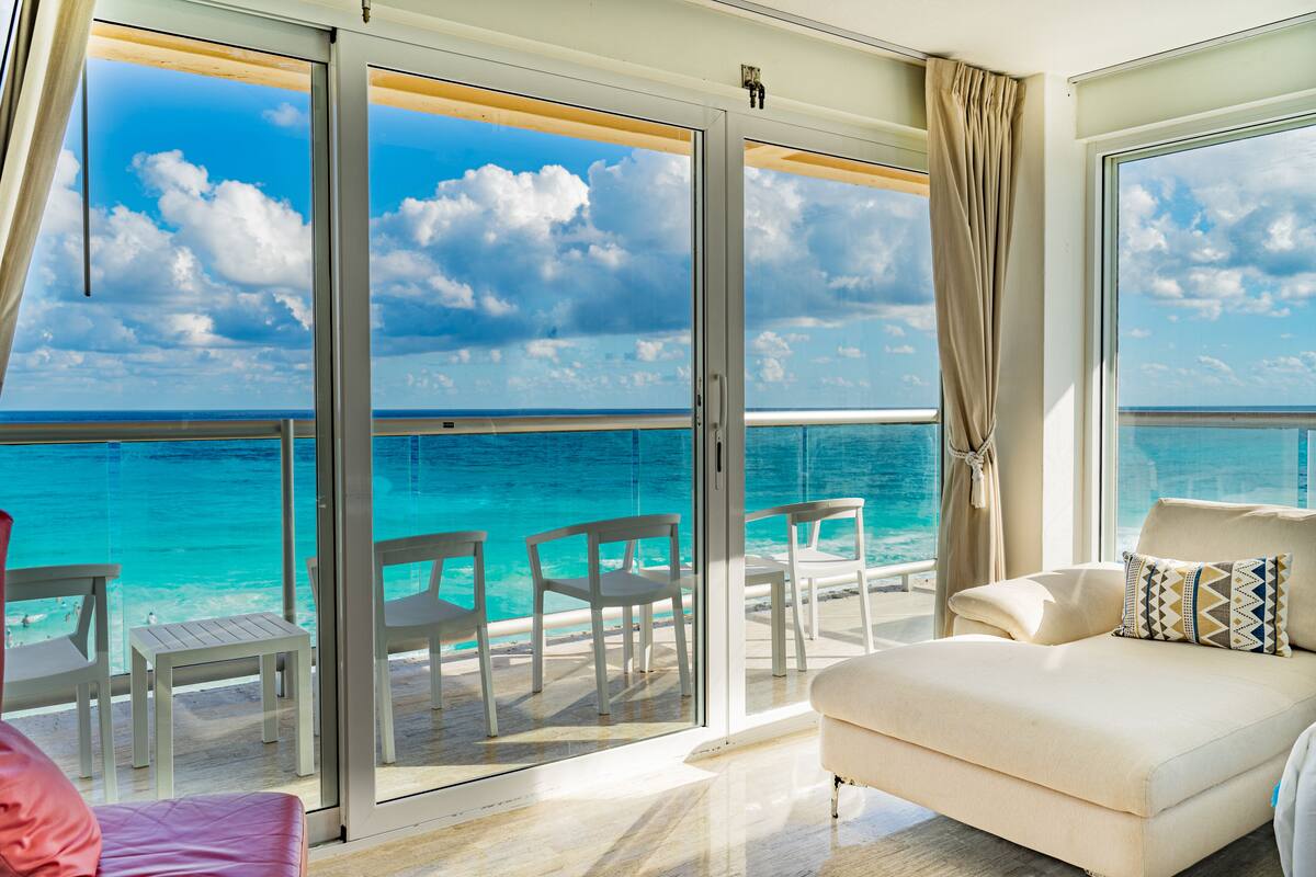 A balcony with a view of the ocean, a white sofa, and several chairs.