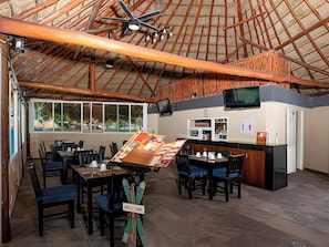 Guests can dine in this cozy dining area with a thatched roof and wooden beams, surrounded by tables and chairs.