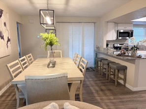 Cozinha moderna com área de jantar, destacando uma ilha central com banquetas, luminária pendente e um vaso com folhagem verde.