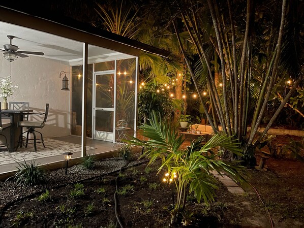 Patio esterno con porta vetrata che dà su un'stanza, circondato da vegetazione rigogliosa e luci decorative.