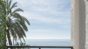 A balcony with a view of the sea, a wooden chair, a small table with a plant, and a potted plant on the left. - Skol Sea Views Apartments (Marbella)