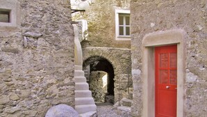 A narrow stone courtyard with a red door, a stone staircase, and a large stone wheel.