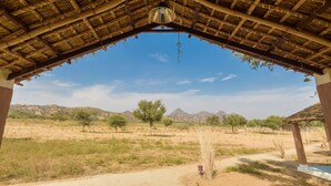 A thatched-roof structure with a view of a desert landscape and mountains in the distance. - Camp Land's End (Pushkar)