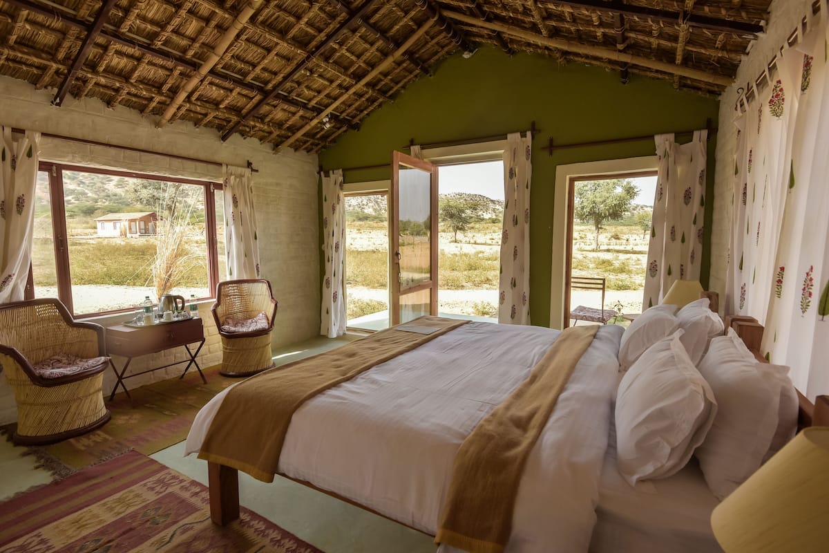 A bedroom with a bed, two wicker chairs, a desk, and a window with curtains.