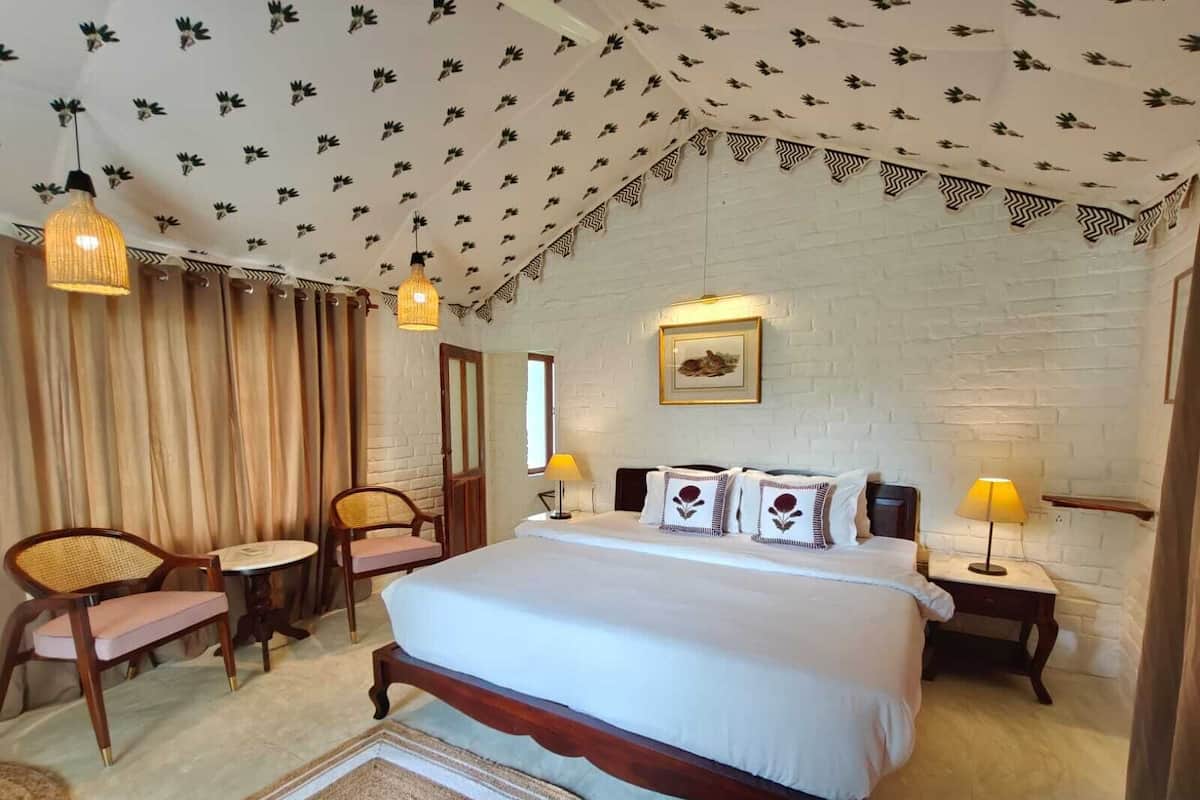A bedroom with a large bed, two bedside tables, a chair, a small table, and a ceiling with a leaf pattern.