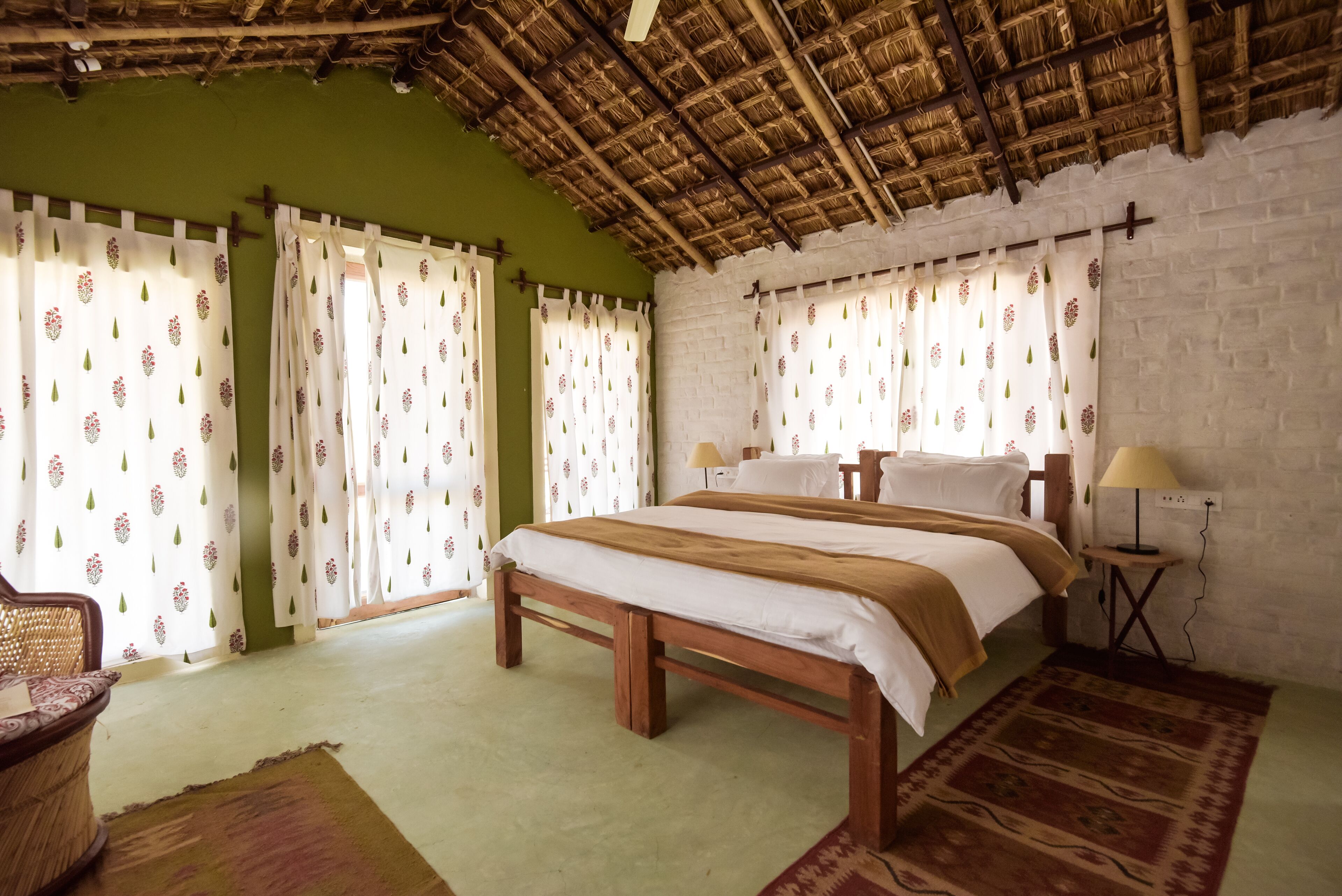 A bedroom with a wooden bed, two bedside tables, a lamp, and a window with curtains.