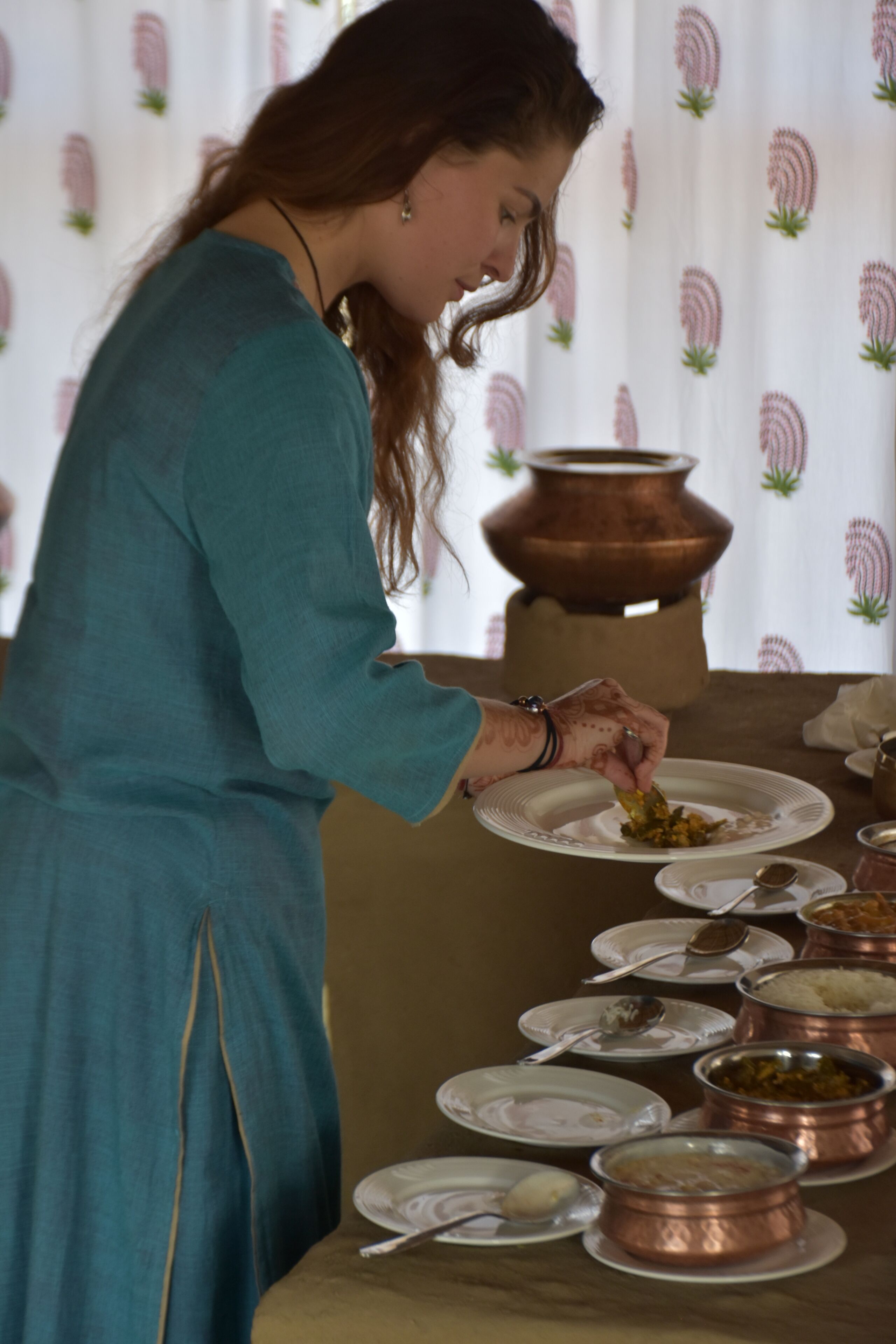 A person serving food from a copper pot on a table with multiple dishes.