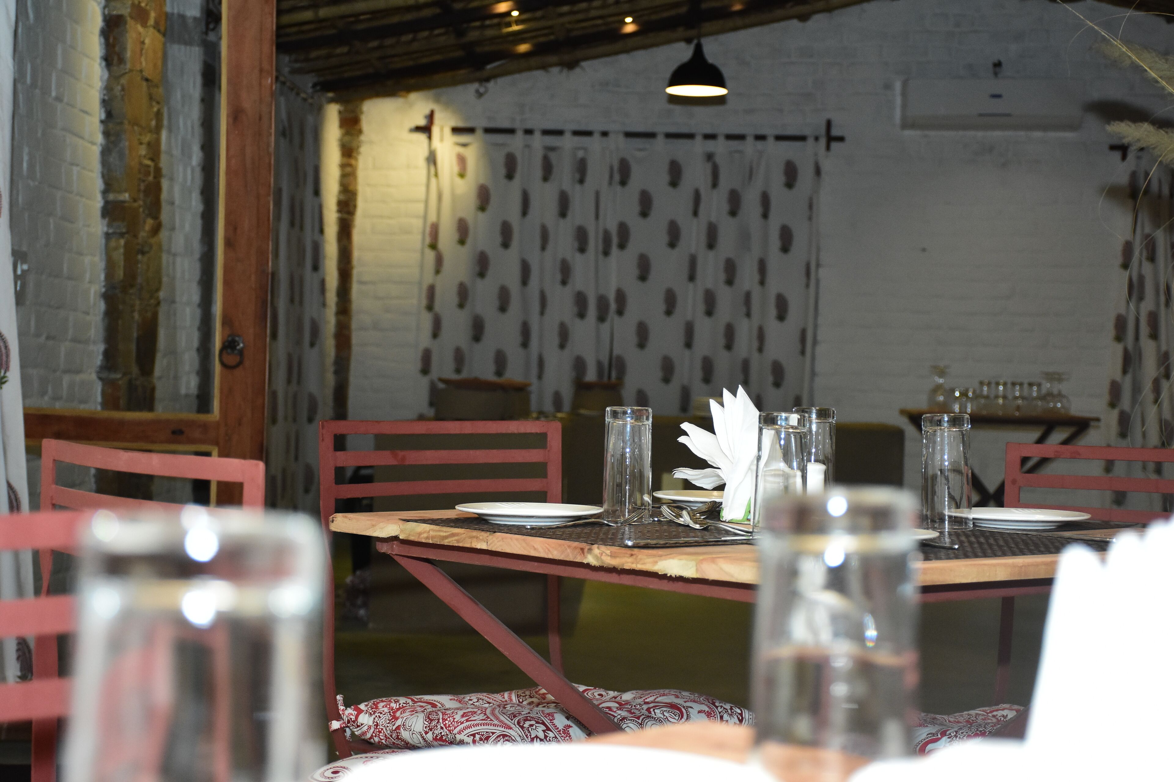 A dining area with a wooden table set for two, red chairs, and a white wall with a polka dot curtain.