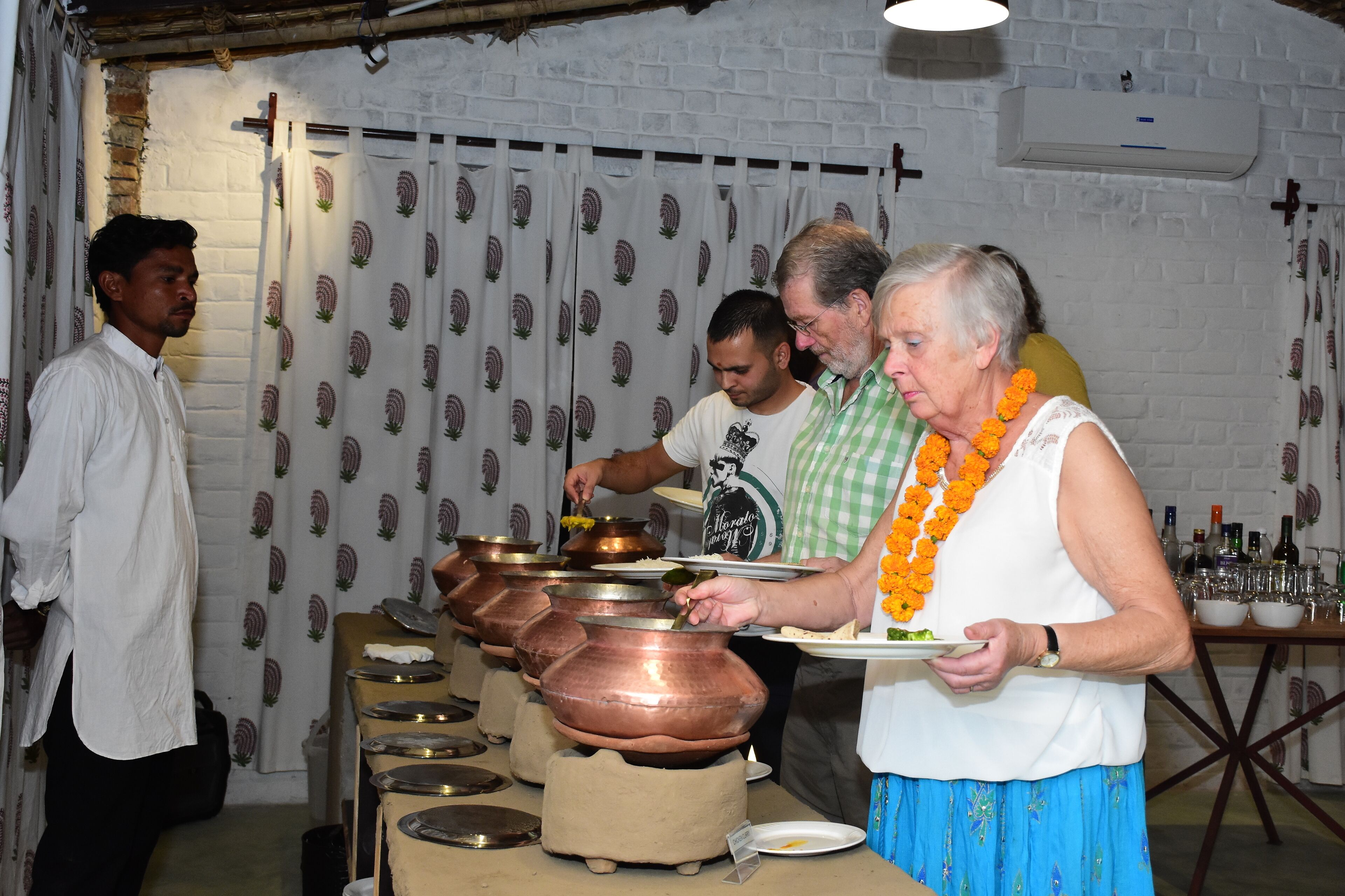 A group of people serving food from copper pots on a table.