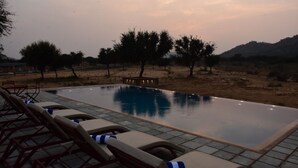 An infinity pool with lounge chairs and a view of a desert landscape. - Camp Land's End (Pushkar)