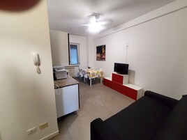 Un ambiente compatto con angolo cottura, zona pranzo e TV su supporto.