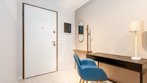 Um quarto com porta fechada, uma escrivaninha com luminária, uma cadeira e um espelho na parede.
