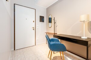 Una stanza con una porta chiusa, una scrivania con una lampada, una sedia e uno specchio sul muro.