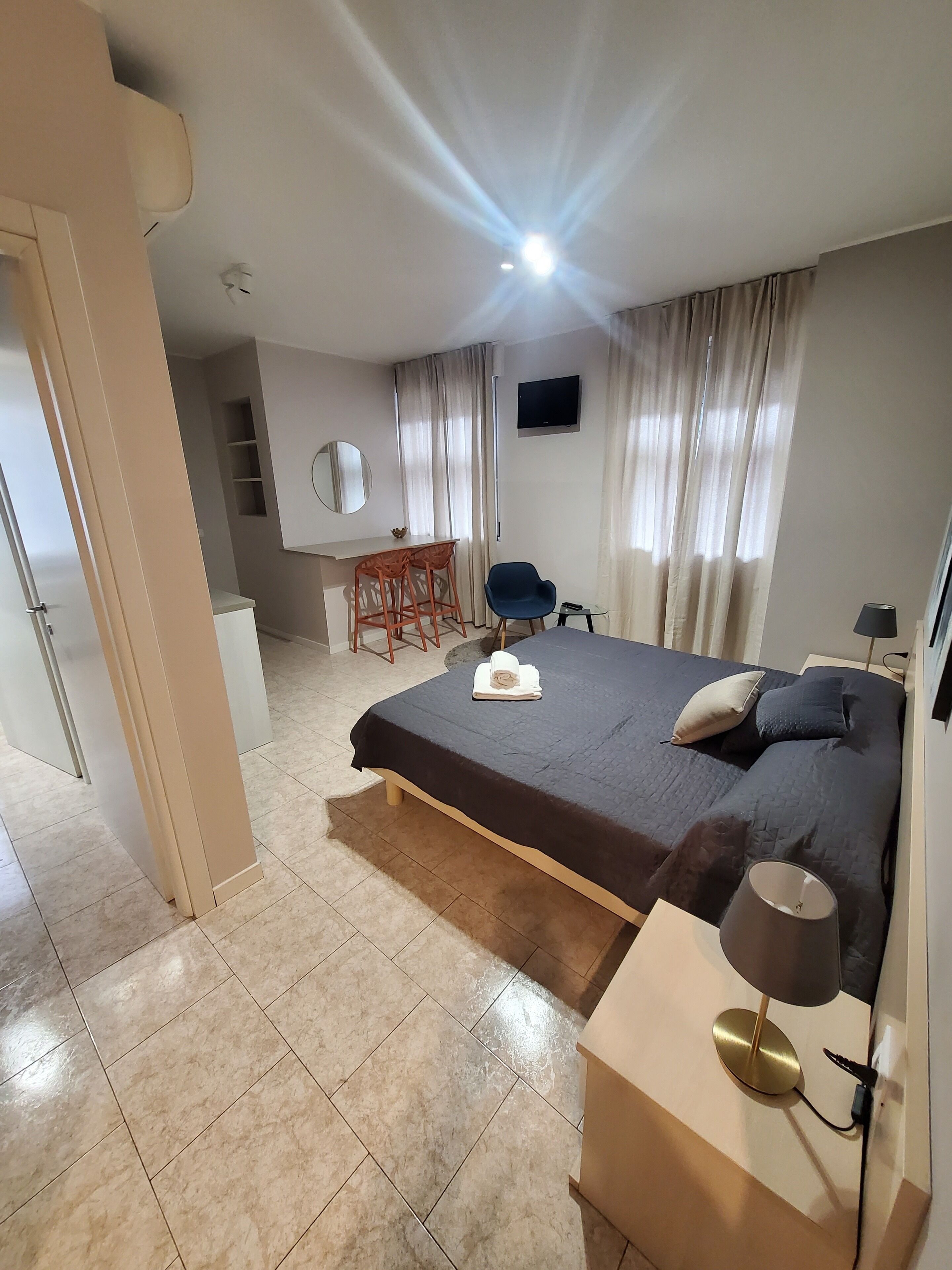 Un dormitorio moderno con cama, mesita de noche, lámpara y un escritorio con sillas.