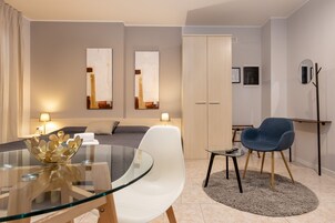 Una camera d'albergo moderna con un tavolo da pranzo in vetro, una sedia blu, un divano e un armadio.