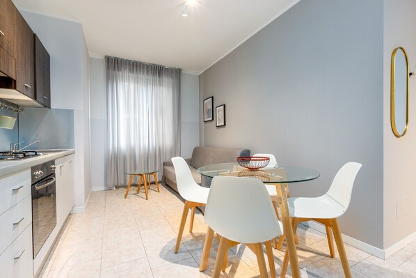 Una cocina moderna con armarios blancos, una estufa a gas y un comedor con mesa de vidrio y sillas blancas.