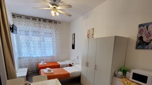 Quarto compacto com uma cama de solteiro, uma mesinha e um guarda-roupa.