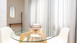 Uma zona de refeições moderna com mesa de vidro, cadeiras brancas, mesa lateral de madeira e um centro de mesa decorativo.