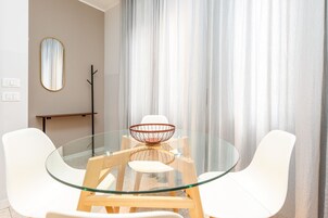 Zona pranzo moderna con tavolo in vetro, sedie bianche, un tavolino in legno e un centrotavola decorativo.