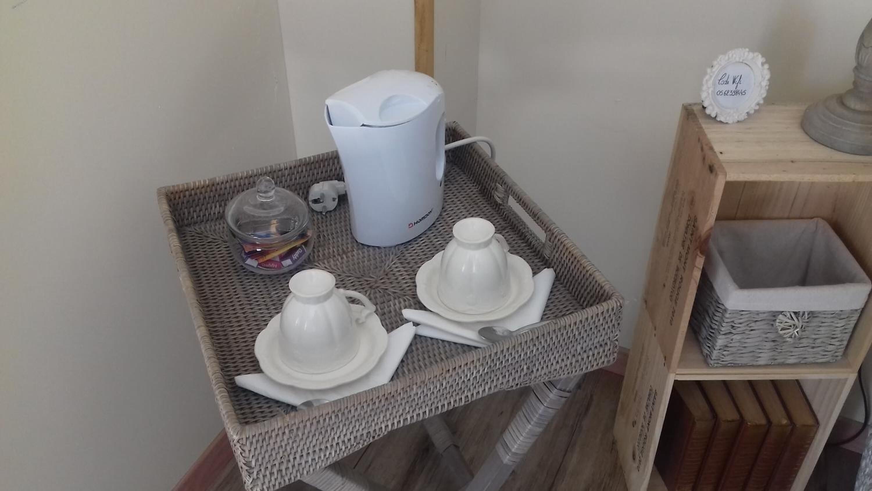 Une petite table en osier sur laquelle se trouvent une cafetière blanche, un bocal en verre et deux théières blanches, le tout disposé sur un plateau.