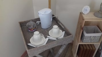Una pequeña mesa de mimbre con una cafetera blanca, un tarro de cristal y dos teteras blancas sobre una bandeja.