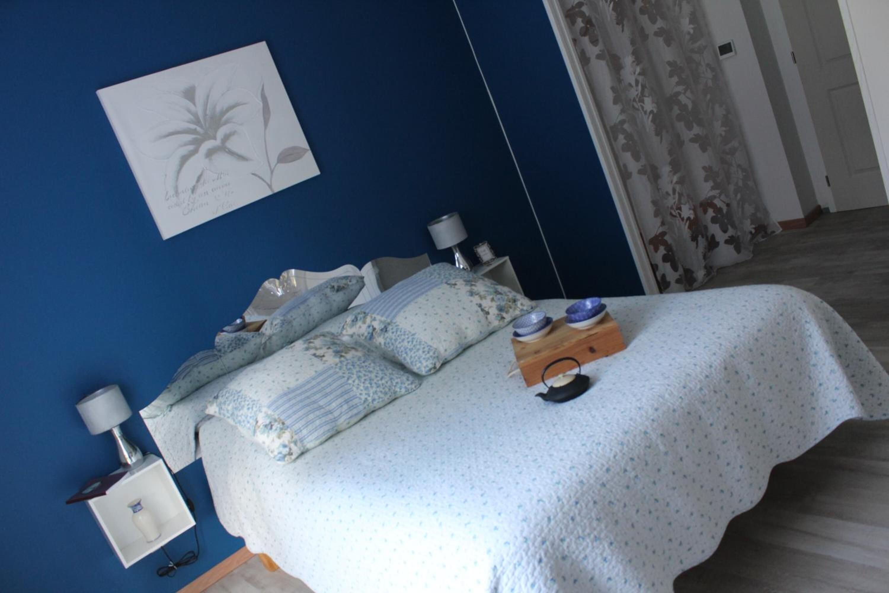 Un dormitorio con cama, almohadas, una mesita de noche con lámpara y un adorno en la pared.