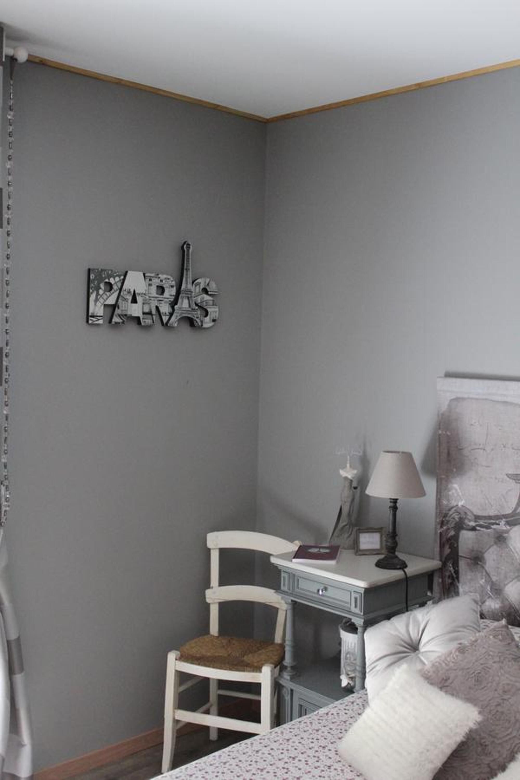 A bedroom with a bed, a desk, a chair, a lamp, and a wall-mounted artwork.