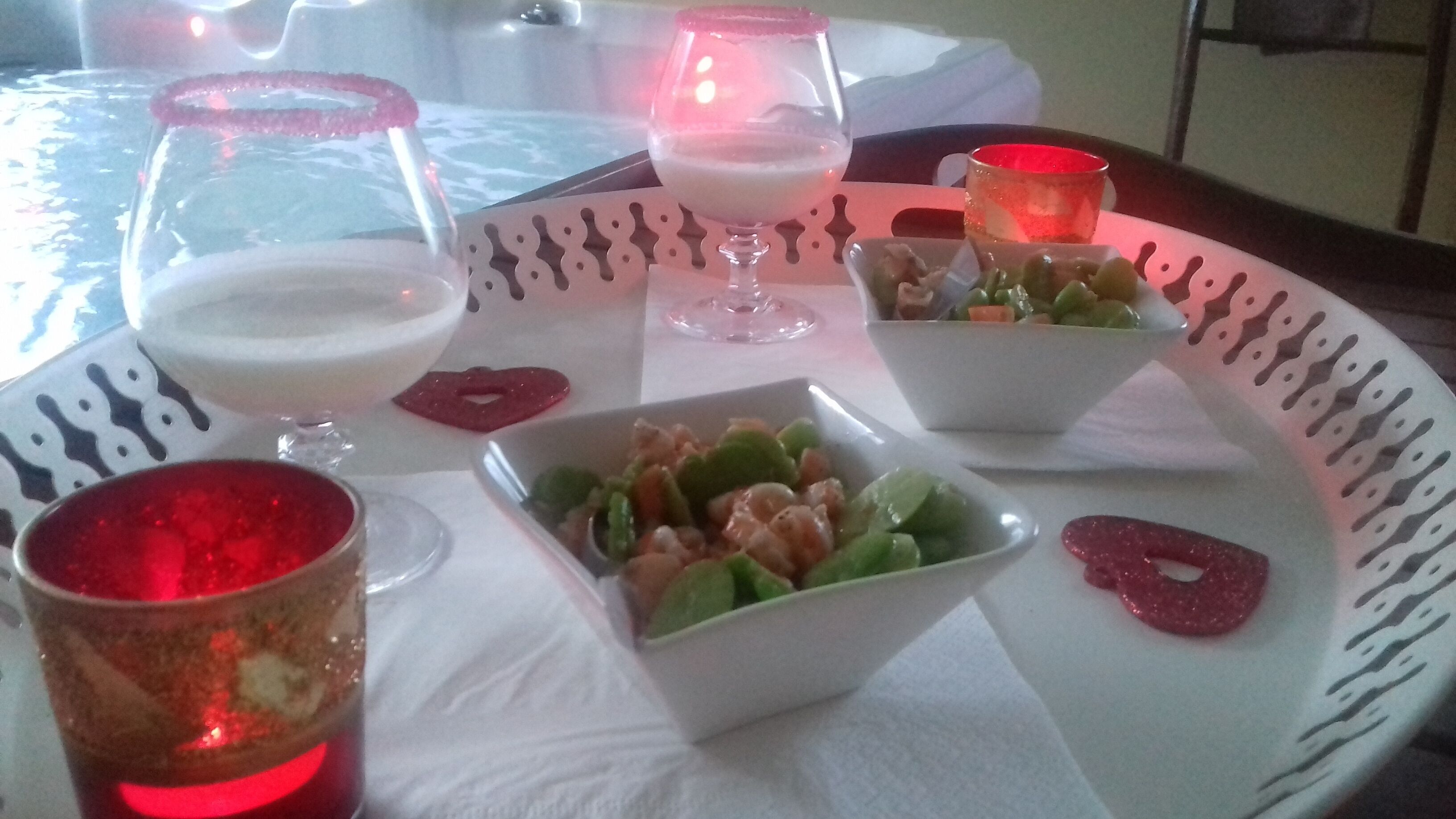 A table with a white plate holding a bowl of fruit salad, a glass of white beverage, and a red drink.