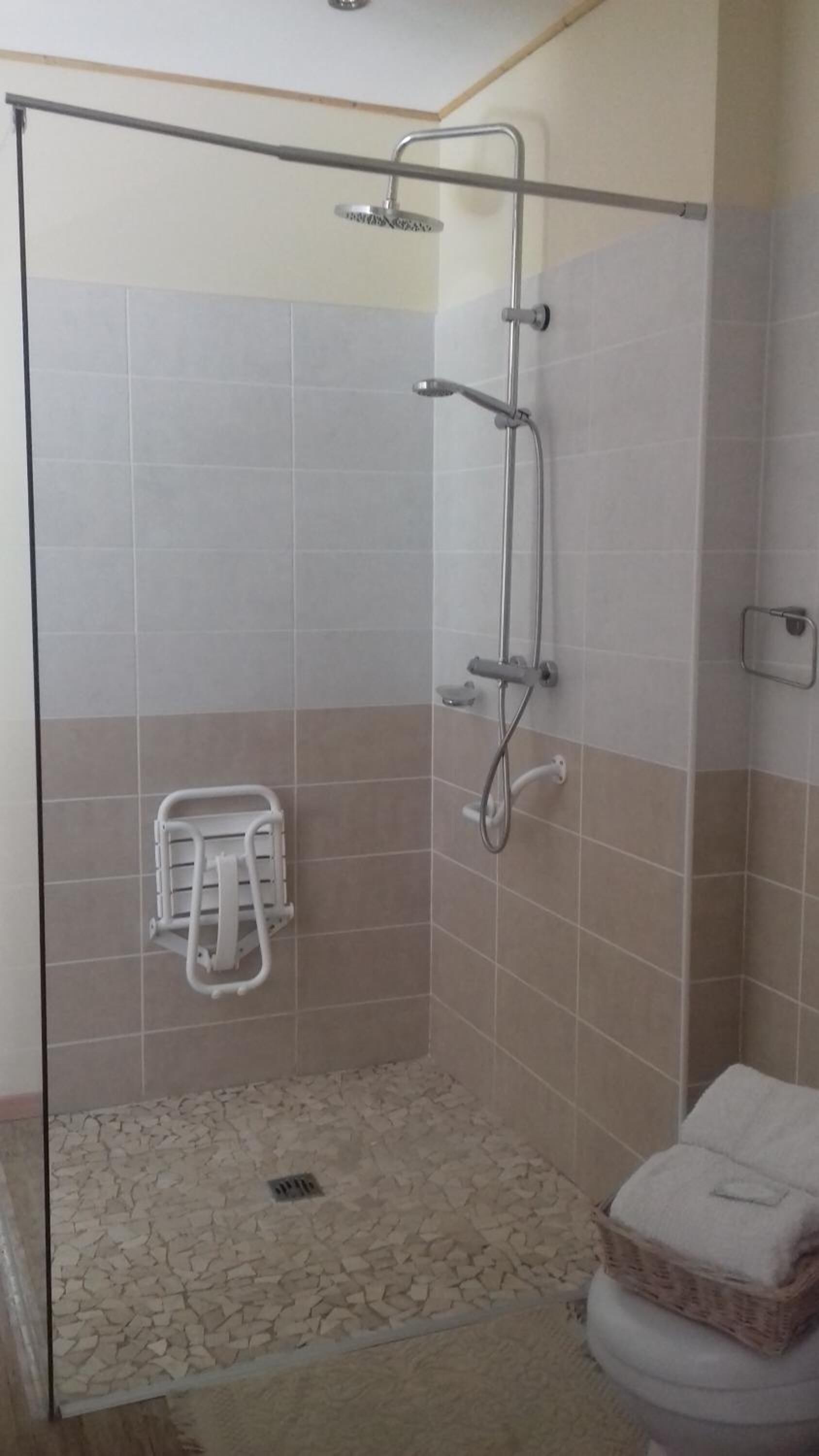 Un espacio de ducha con paredes de vidrio, una toalla blanca y una cesta en el suelo.