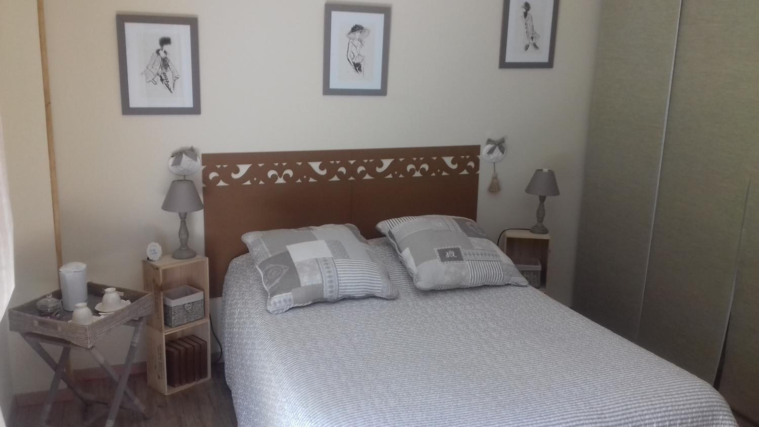 Un dormitorio ordenado con una cama, dos mesitas de noche, una mesita auxiliar y tres cuadros enmarcados en la pared.