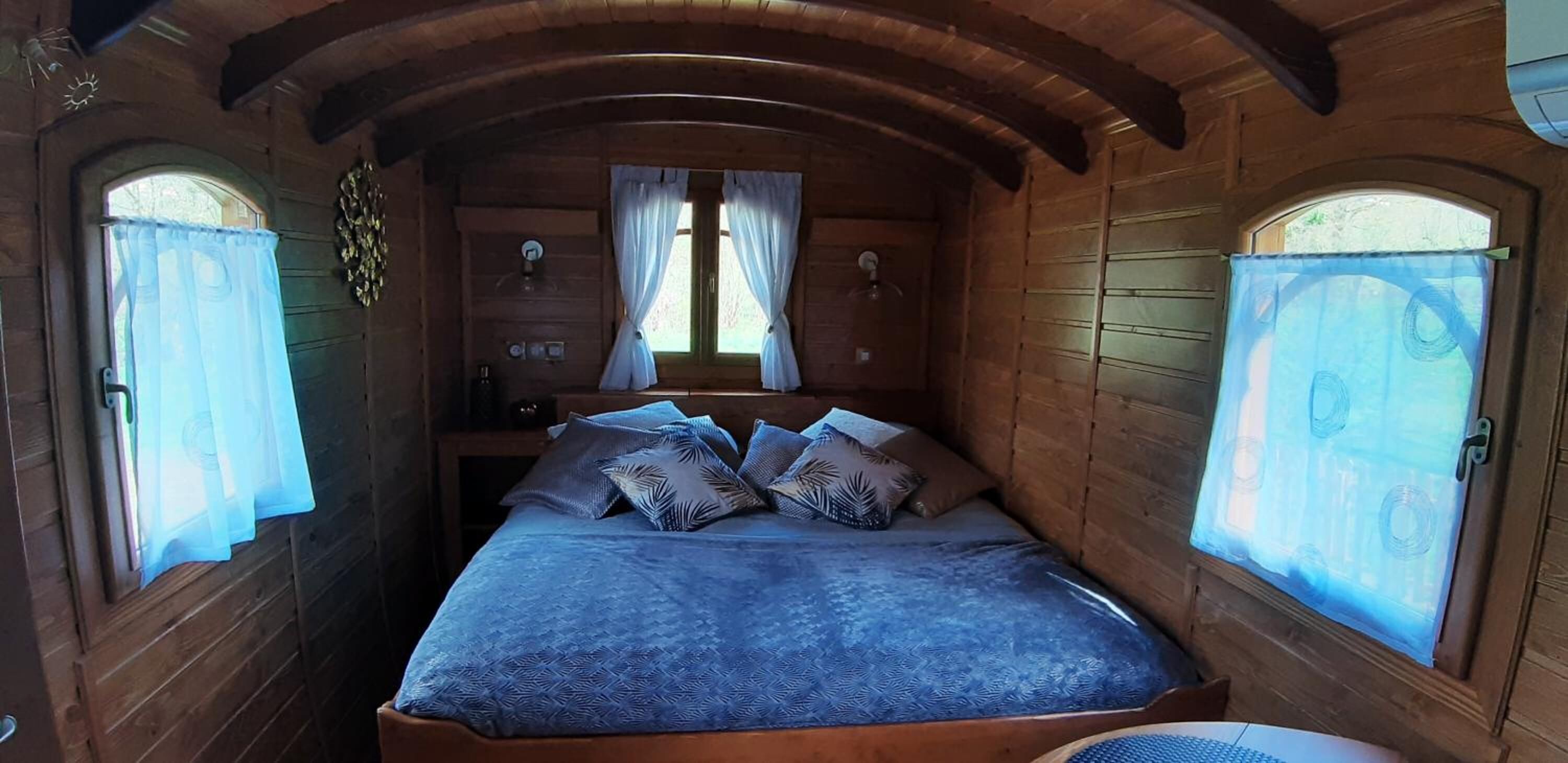 Een gezellig houten kamer met een bed, twee raamdecoratie en een klein tafeltje.