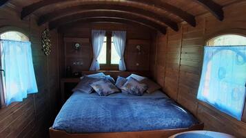 Een gezellig houten kamer met een bed, twee raamdecoratie en een klein tafeltje.