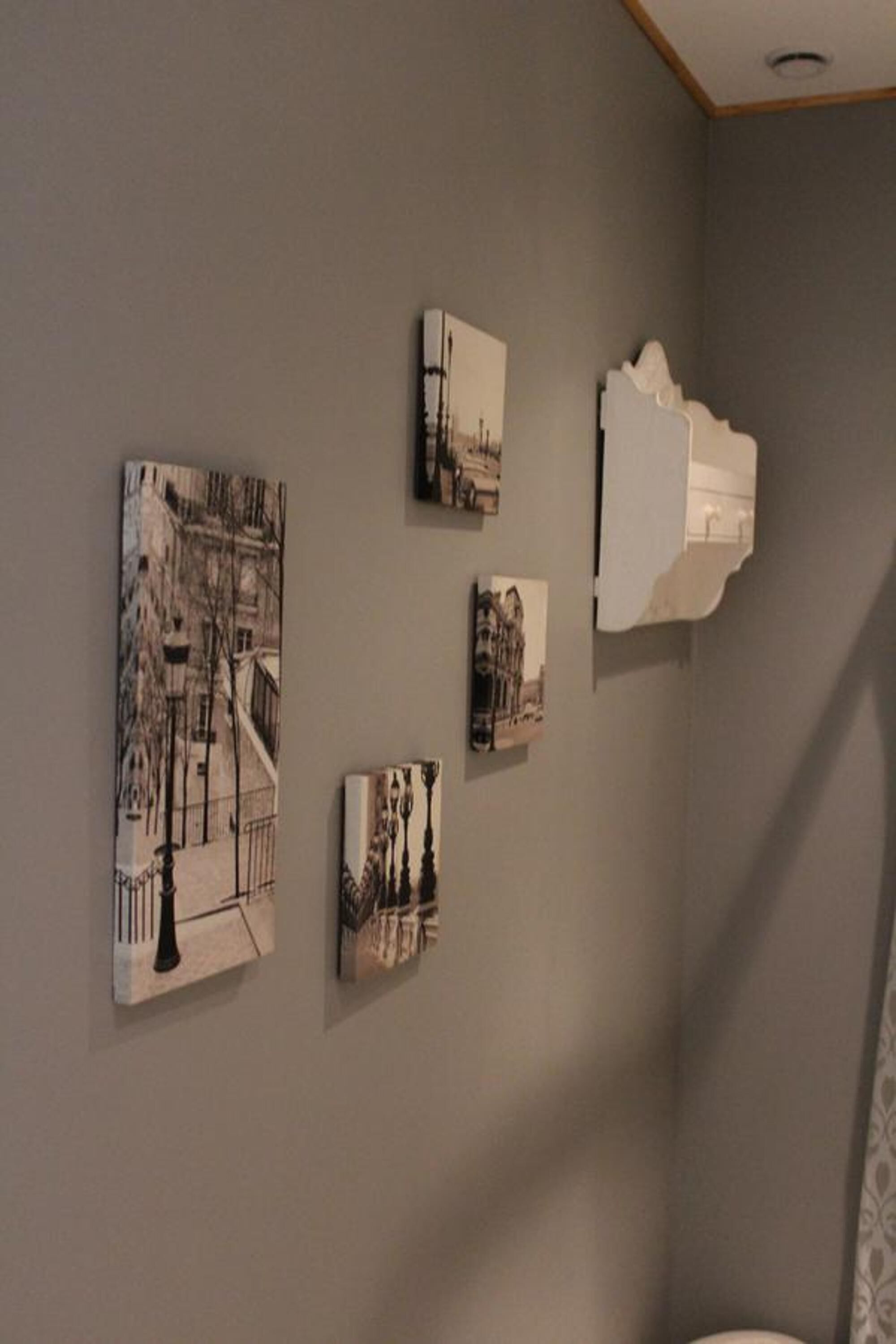 A room with a grey wall and a ceiling with a wooden trim. There are four framed pictures on the wall, depicting various architectural scenes.