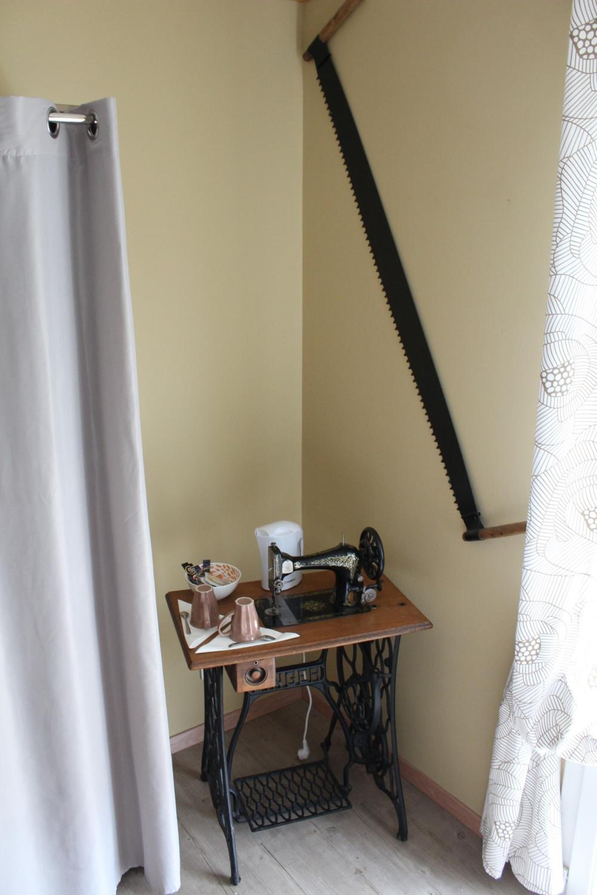 Una habitación de esquina con una máquina de coser antigua sobre una mesa de madera, un tazón pequeño y una taza.