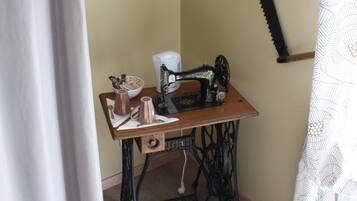 Una habitación de esquina con una máquina de coser antigua sobre una mesa de madera, un tazón pequeño y una taza.