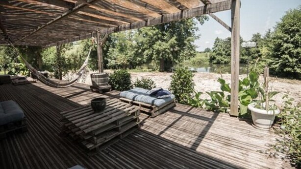 Een terras buiten met houten vloer, een hangmat en zitgedeeltes.
