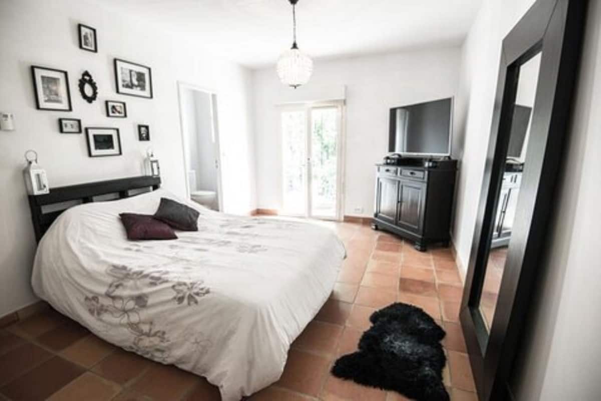 A bedroom with a bed, a dresser, a TV, and a mirror.