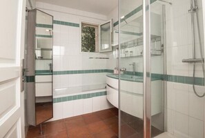 A bathroom with a glass-enclosed shower, white tiles with green stripes, a window, and a mirror. - La Villa Bella (Abzac)