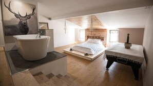 Een slaapkamer met een groot bad, een bed met houten hoofdeinde en een schilderij van een hert op de muur.