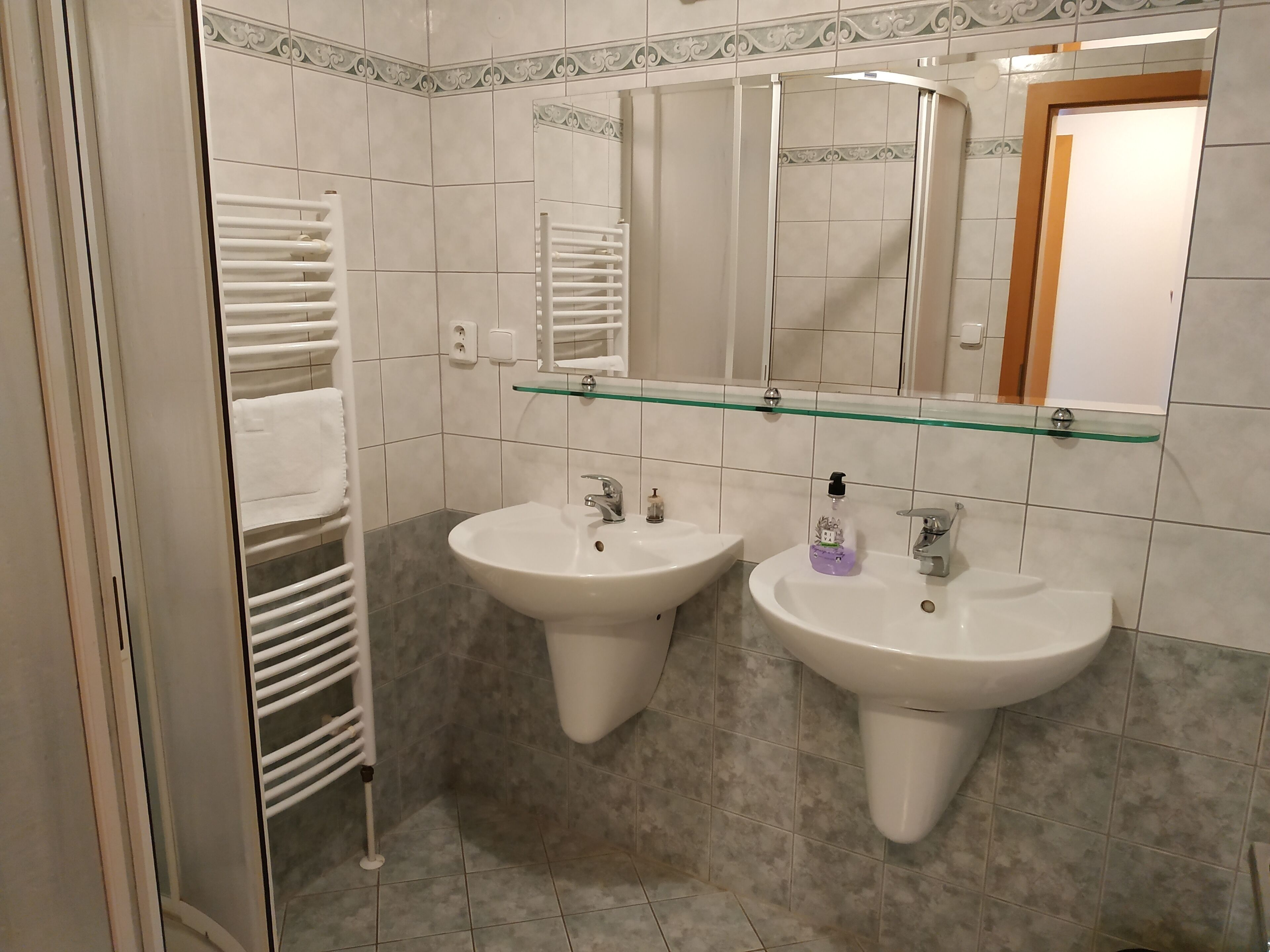 A bathroom with two sinks, a glass shelf above, and a towel rack.