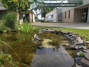 Un estanque bordeado de piedra, rodeado de follaje y un edificio con entrada de vidrio.