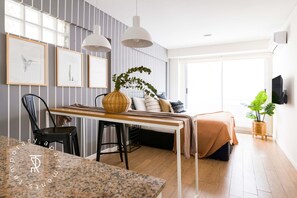 A modern living room with a dining area, a sofa, a TV, and a large window.