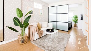Una sala de estar moderna con un sofá blanco, una planta grande en maceta, una mesa de centro redonda y un ventanal con vistas.