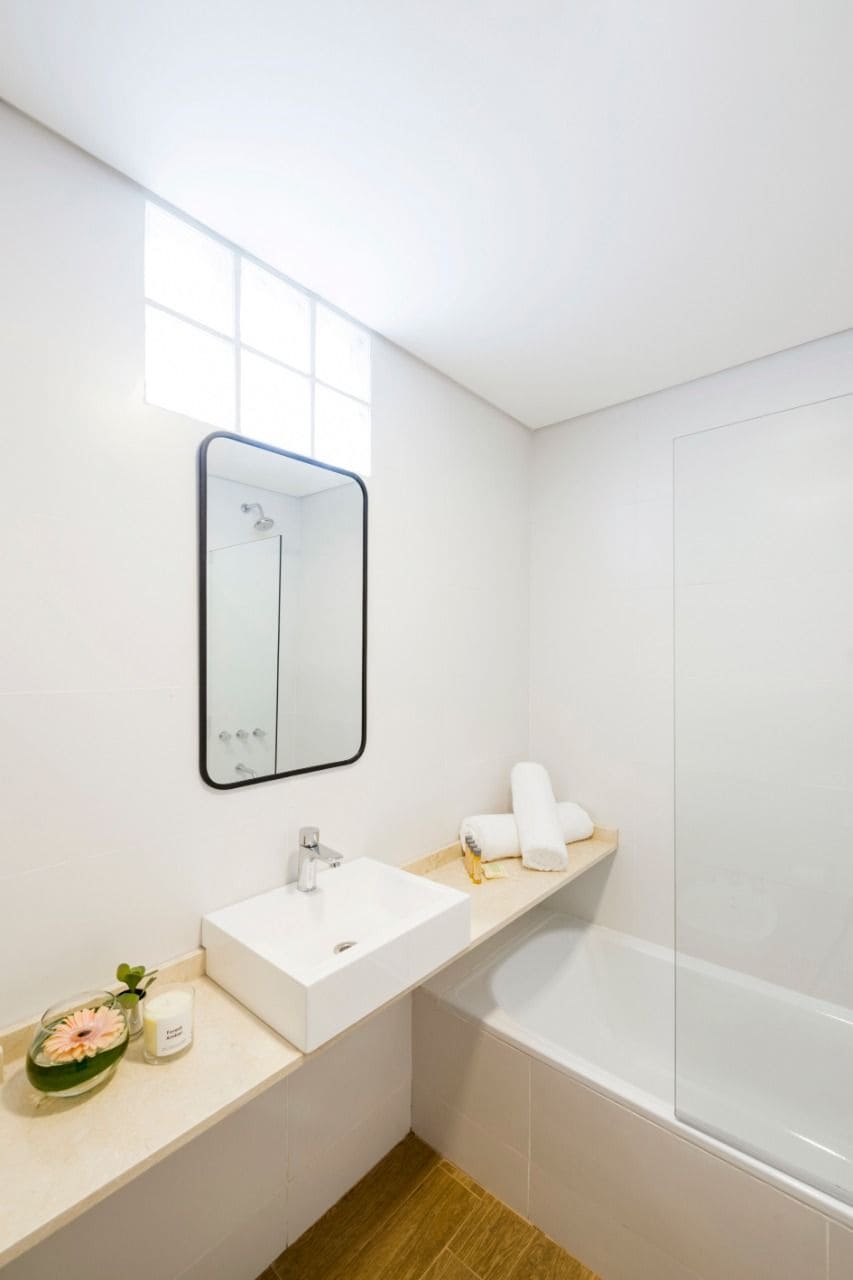 Un baño moderno con lavamanos, espejo y bañera blancos.