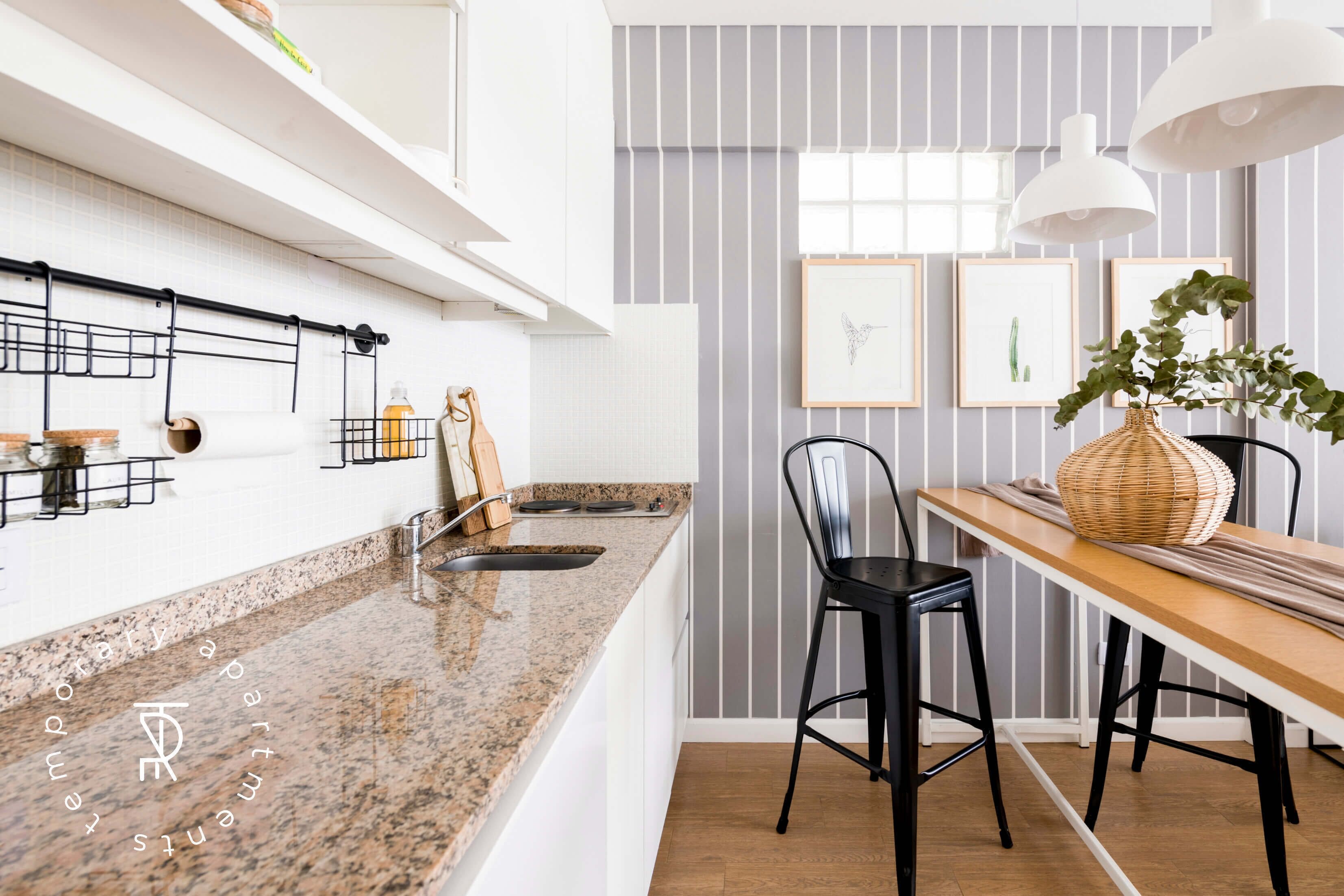 Een moderne keuken met granieten aanrecht, een houten eettafel, zwarte barkrukken en een hanglamp.