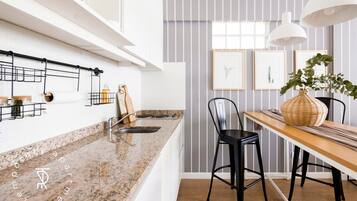 Een moderne keuken met granieten aanrecht, een houten eettafel, zwarte barkrukken en een hanglamp.