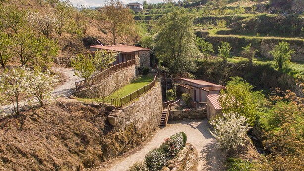 Un edificio de paredes de piedra con un jardín en terrazas y una escalera que lleva a una terraza de madera.
